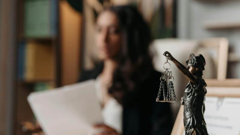 Close-up of a justice figurine on desk with blurred female lawyer in office setting.